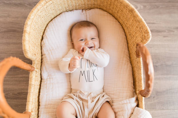 A Happy 14 Week Old Baby Boy Wearing a White Onesie With the Words 'But First Milk' Laying in a Cozy Cream Cotton Blanket in a Seagrass Moses Basket A 14 Week Old Baby Boy Wearing a White Onesie With the Words 'But First Milk' Laying in a Cozy Cream Cotton Blanket in a Seagrass Moses Basket moses basket stock pictures, royalty-free photos & images