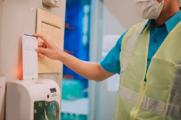 Close up Asian Chinese blue collar worker clock in with time card punching in the morning