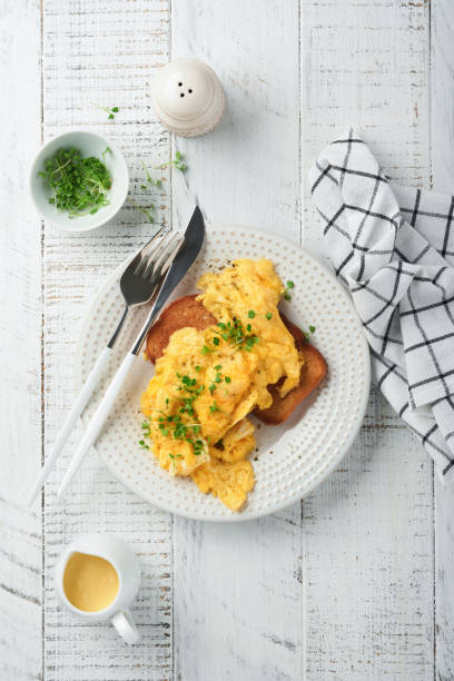 istock Scrambled Eggs. Fluffy and Buttery scrambled eggs on bread with microgreen radish and hollandaise sauce on white plate over white wooden background. Homemade breakfast or brunch meal. Top view. 1388791263