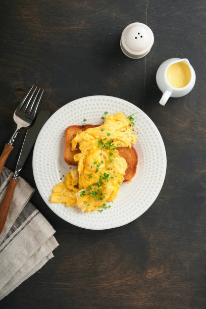 istock Scrambled Eggs. Fluffy and Buttery scrambled eggs on bread with microgreen radish and hollandaise sauce on white plate over dark old wooden background. Homemade breakfast or brunch meal. Top view. 1388791401