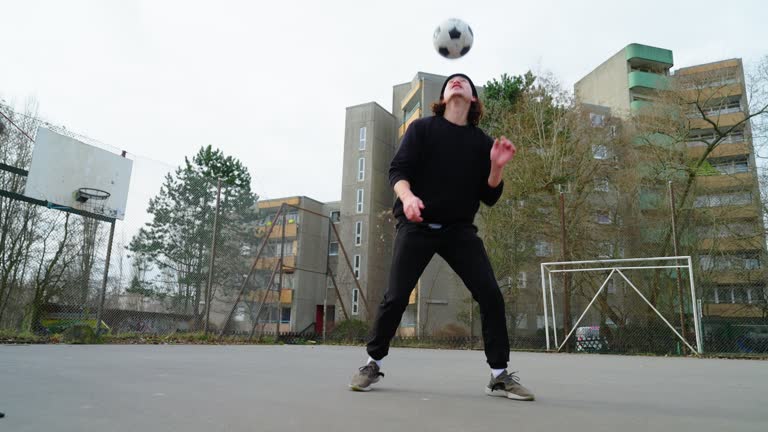 Young man juggles football on leg at urban soccer court