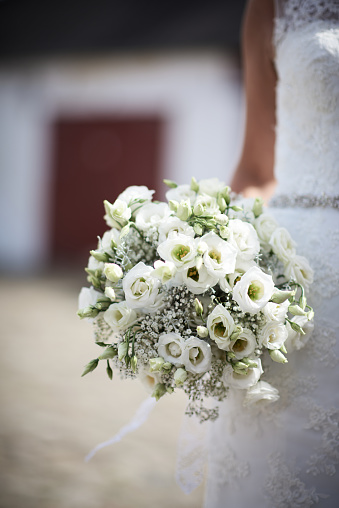 Midsection of bride wearing dress holding bouquet of white roses while standing in wedding ceremony