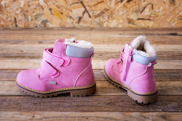 Pair of pink colored kids leather boots on wood background