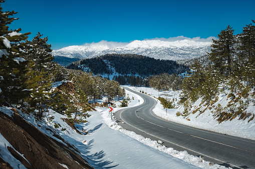 Open air, asphalt paved clean road between successive hills and mountains. Surrounded by snow