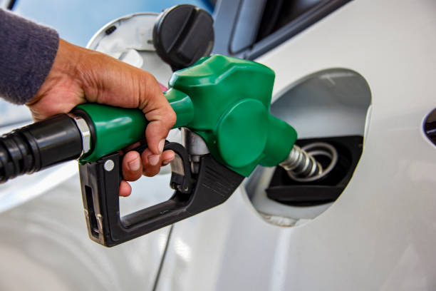 man handle pumping gasoline fuel nozzle to refuel. vehicle fueling facility at petrol station. white car at gas station being filled with fuel. transportation and ownership concept - petrol imagens e fotografias de stock