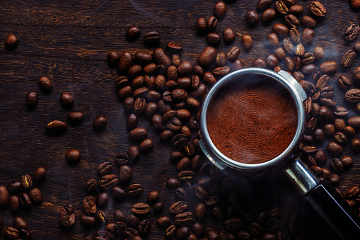 White coffee cup and coffee beans on burlap textile and brown background.