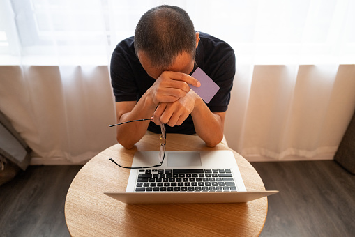 Asian man looking down and sitting in front of his laptop looking depressed