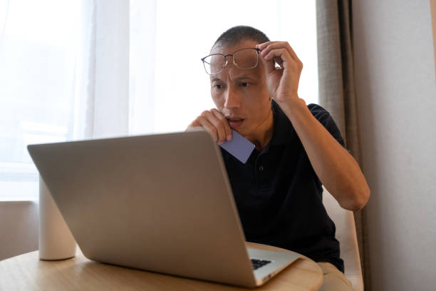 Asian man looking at laptop screen in amazement Asian man looking at laptop screen in amazement consumer confidence photos stock pictures, royalty-free photos & images
