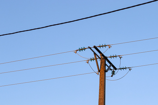 Overhead power lines with exposed cables, on blue sky.