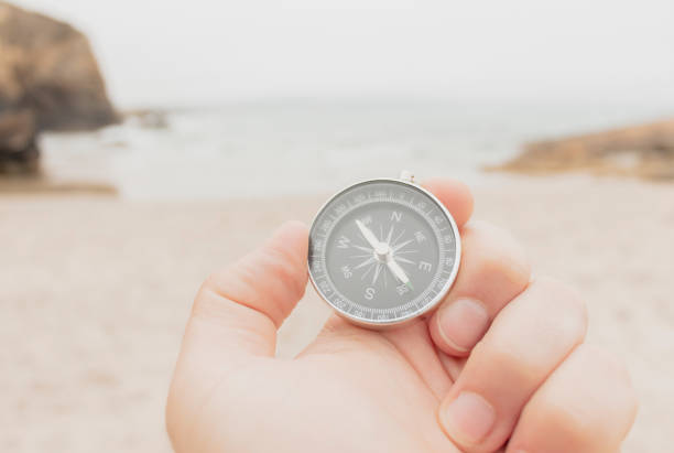 mano sosteniendo una brújula en la playa frente al mar - compass exploration the way forward beach fotografías e imágenes de stock