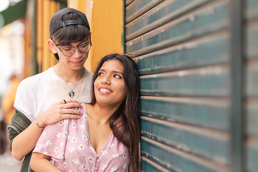 Portrait with copy space of a teen couple smiling and looking each other next to a urban garage wall