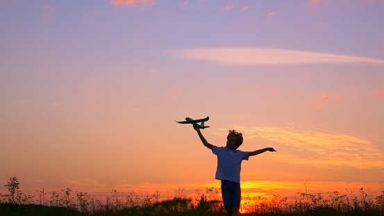A teenage boy in the rays of the setting sun has fun playing with an airplane in the backyard. Dreams of becoming a pilot and flying like a bird. Children's happy life