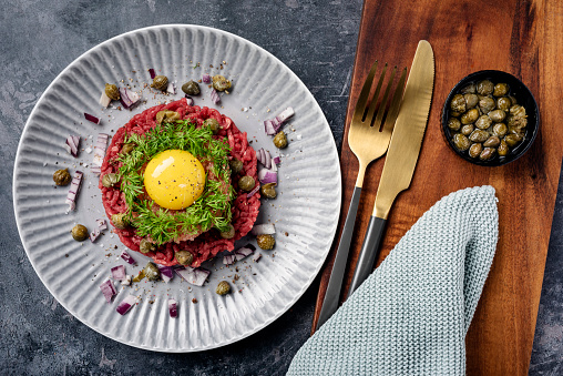Overhead view of a plate of steak tartare with; capers, red onion, dill and lump fish caviar or “stenbiderrrogn” in danish served with the obligatory raw egg. A real luxury experience, colour, horizontal format.