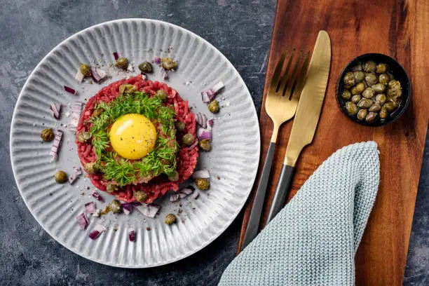 Overhead view of a plate of steak tartare with; capers, red onion, dill and lump fish caviar or “stenbiderrrogn” in danish served with the obligatory raw egg. A real luxury experience, colour, horizontal format.