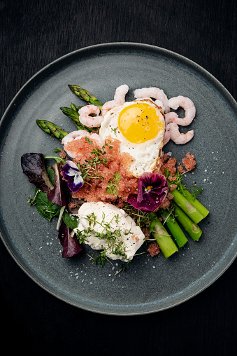 Overhead view of lumpfish caviar served with creme fraiche dressing, fresh asparagus, prawns, salad leaves and topped off with a fried quails egg. Lumpfish caviar is a seasonal delicacy in Denmark in the early spring known as “stenbiderrogn”. A real luxury experience, colour, vertical format with some copy space.
