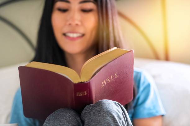 Smiling East Asian woman reading the Bible at home stock photo
