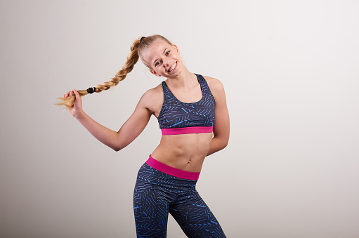 Portrait of smiling young woman wearing sports clothing holding braided hair while standing against white wall at home