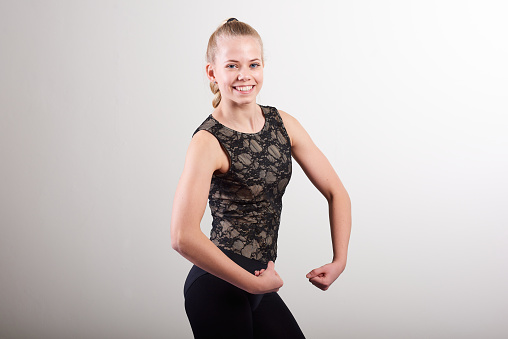 Portrait of smiling young woman wearing black clothing flexing muscles while standing against white wall