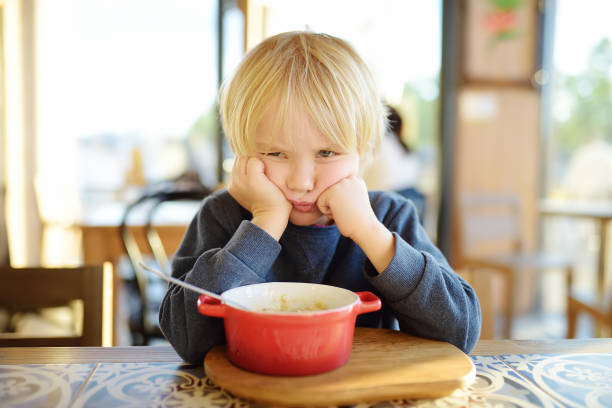 Little child sitting the table in cafe or restaurant and doesn't want to eat. Healthy food. Kids diet. Poor appetite. stock photo