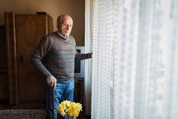 istock Senior man using walking cane to stand by the window 1388819789
