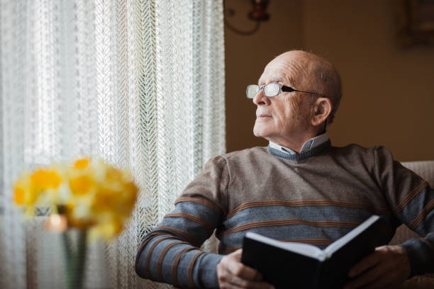 istock Old man with a book looking through the window 1388819834