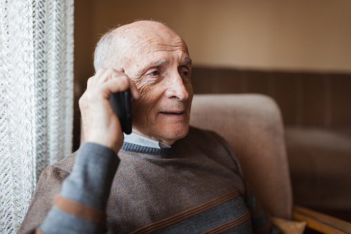 Nostalgic senior man using smart phone and talking with his family, close-up