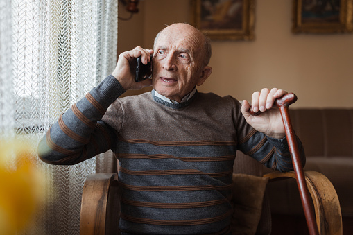 Older man looking in distance when using smart phone to talk with family