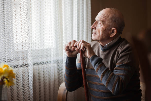 istock Senior man looking through the window and leaning onto a stick 1388820032
