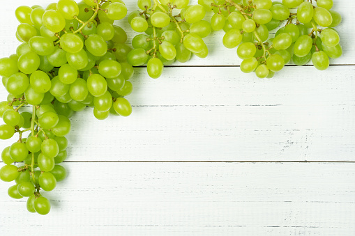 Frame from bunch of green grapes on white wooden background with empty space for text.