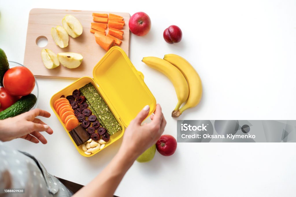 Young woman making school healthy lunch in the morning. Close up on pair of young female hands preparing vegan breakfast and a snack for school for her children. Top view. Concept healthy food for schoolchild Lunch Box Stock Photo