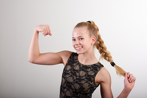 Portrait of happy young woman with braided long hair flexing muscle while standing against white wall