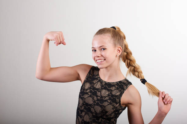 Portrait of woman with braided hair flexing muscle against wall stock photo