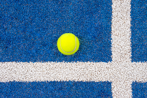 PADEL TENNIS BALL ON BLUE COURT NEXT TO WHITE LINES. TOP VIEW.