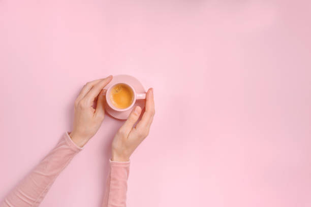 istock Female hands holding a cup of coffee on pink background 1388836734
