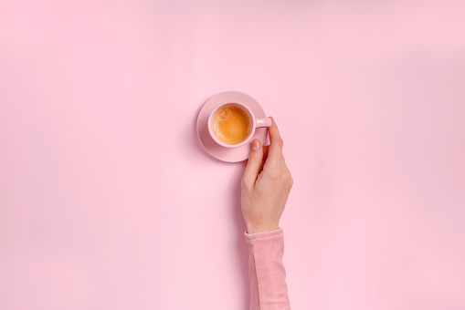 Woman's hand holding a cup of espresso on pink background