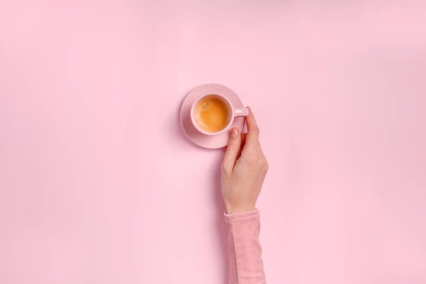 Woman's hand holding a cup of coffee on pink background stock photo