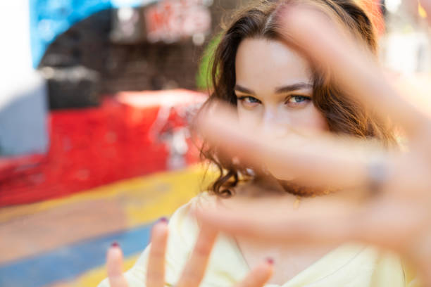 Beautiful lady in yellow summer costume making selfie using smartphone. Sitting on the background with colorful tropical pattern. Concept of summer holidays. Cool look fashionable city street outfit.