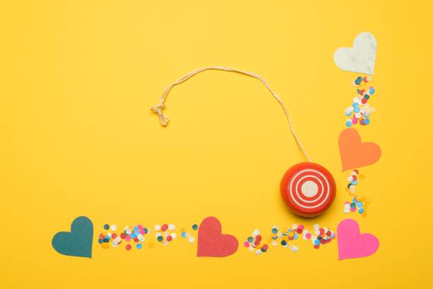 High angle view of yo-yo on yellow color background with colored heart shape cardboards and colored confetti papers.