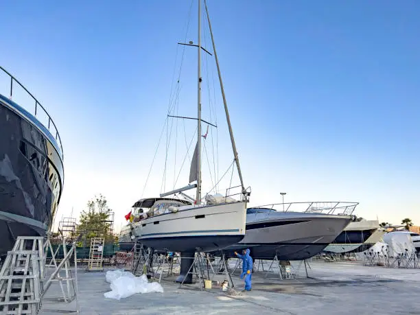 In a row private yachts have been lifted for maintenance and painting works at Karaada Marina in Bodrum dry dock a sunny evening with blue sky.  Professional occupation and service at shipyards