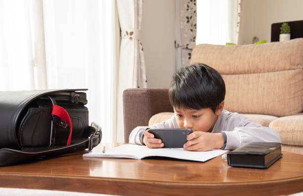 elementary school boys looking at smartphones while studying - homework pencil people indoors imagens e fotografias de stock