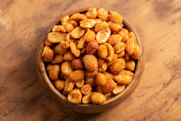 a bowl of honey roasted peanuts on a dark wooden table - beer nuts imagens e fotografias de stock