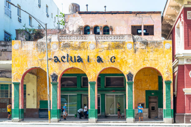 Havana, Cuba - March 16, 2022: Cuban people under a porch of an old building with a sign reading 'actualidades' (some missing letters). They are wearing face masks