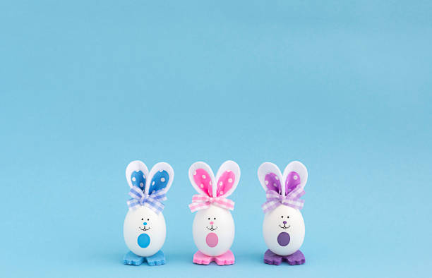 istock Three white eggs with painted eyes and multi-colored ears on a blue background in the center. copy space 1388852436