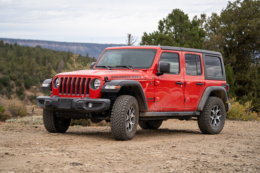 Red Jeep Wrangler Rubicon parked on a dirt road in the Colorado wilderness with overcast sky. View from front angle. Photo taken in Telluride, Colorado.