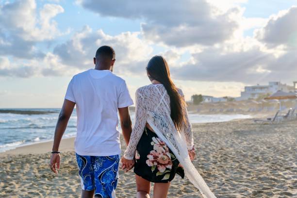 istock Young happy couple walking on the beach holding hands, back view. 1388854057