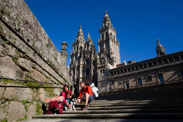 two pilgrims finish the camino de santiago and rest on the steps of plaza del obradoiro in front of the cathedral of santiago de compostela - chinese temple dog imagens e fotografias de stock