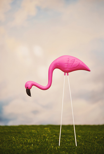 Bright pink flamingo yard ornament in grass with sky of clouds in the background