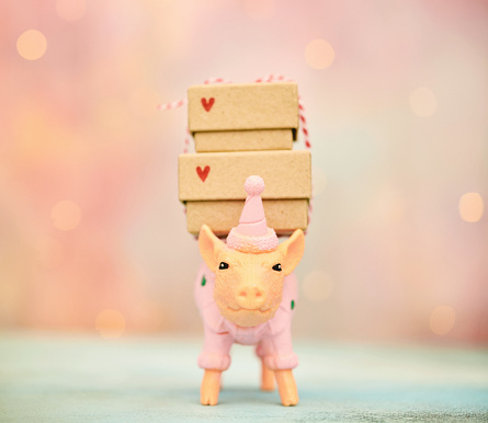 Cute plastic pig dressed in a pink sweater and party hat carrying a stack of gifts