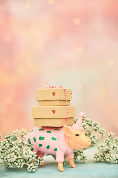 Cute plastic pig dressed in a pink sweater and party hat carrying a stack of gifts
