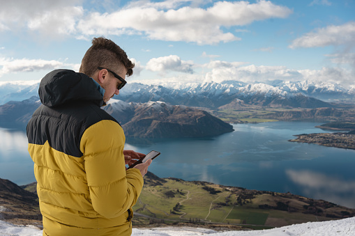 Man with using smartphone in mountain summit. Roy's Peak, Wanaka, New Zealand landscape